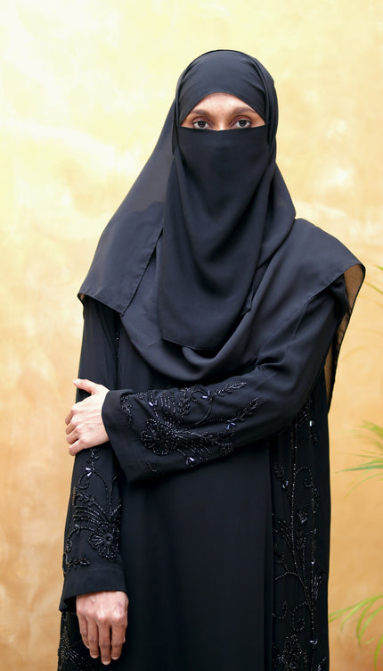 Person wearing a black abaya with intricate designs on a gold background