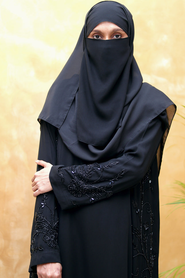Person wearing a black abaya with intricate designs on a gold background