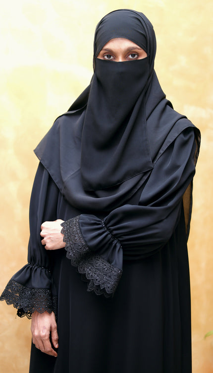 Person wearing a black abaya with lace cuffs on a beige background