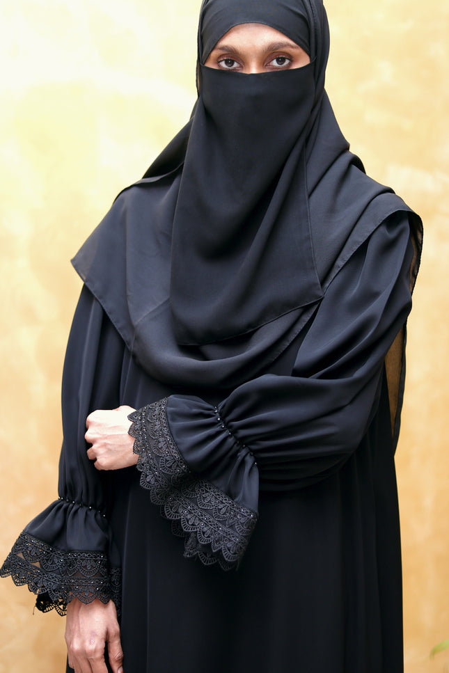 Person wearing a black abaya with lace cuffs on a beige background