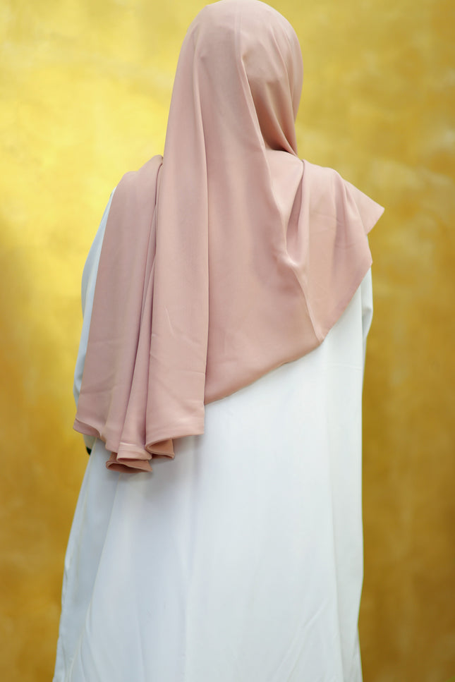 Person wearing a pink hijab and white outfit against a yellow background