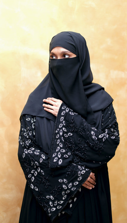 Person wearing a black embroidered hijab against a beige background