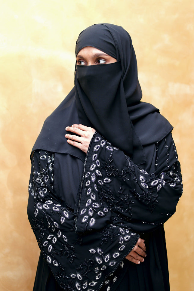 Person wearing a black embroidered hijab against a beige background