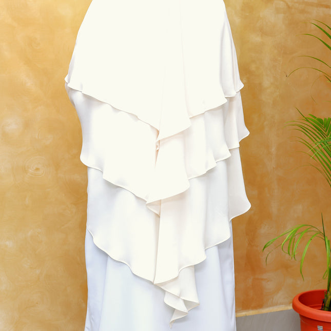 White ruffled garment on a mannequin against a beige wall with a plant in the corner.