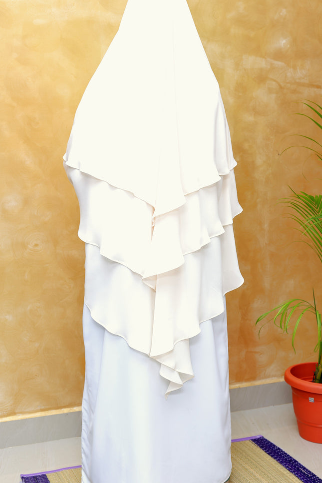 White ruffled garment on a mannequin against a beige wall with a plant in the corner.