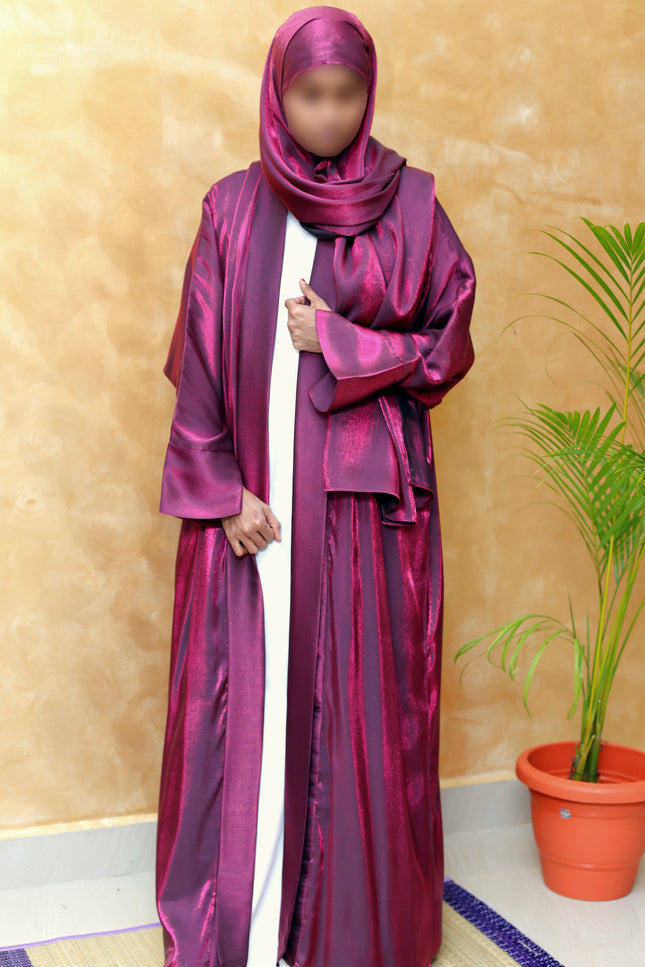 Person wearing a magenta abaya with a matching hijab against a beige wall.