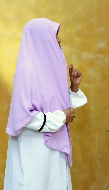 Person wearing a light purple hijab and white outfit against a yellow background
